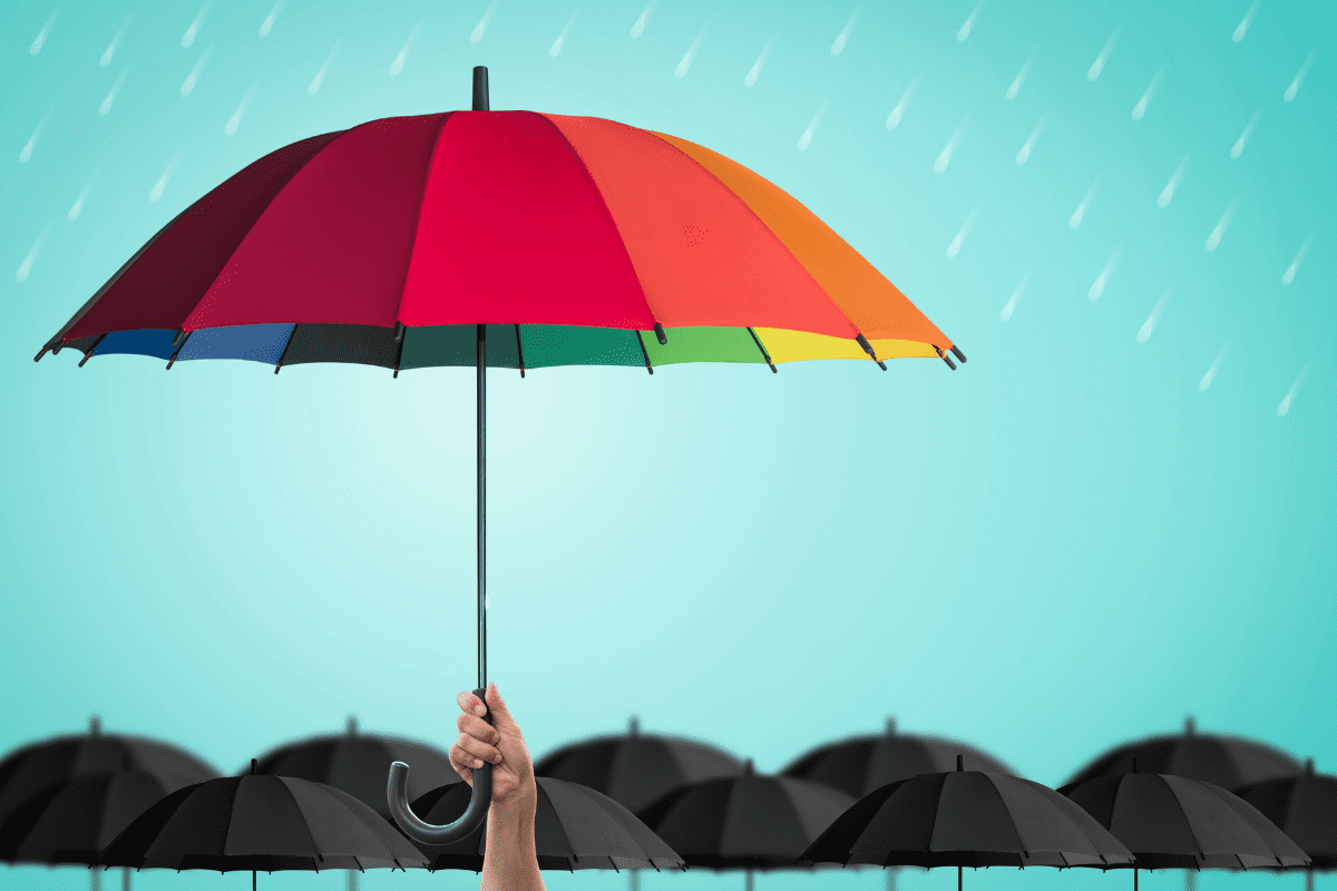 photo of a rainbow-coloured umbrella in front of several black umbrellas in the background
